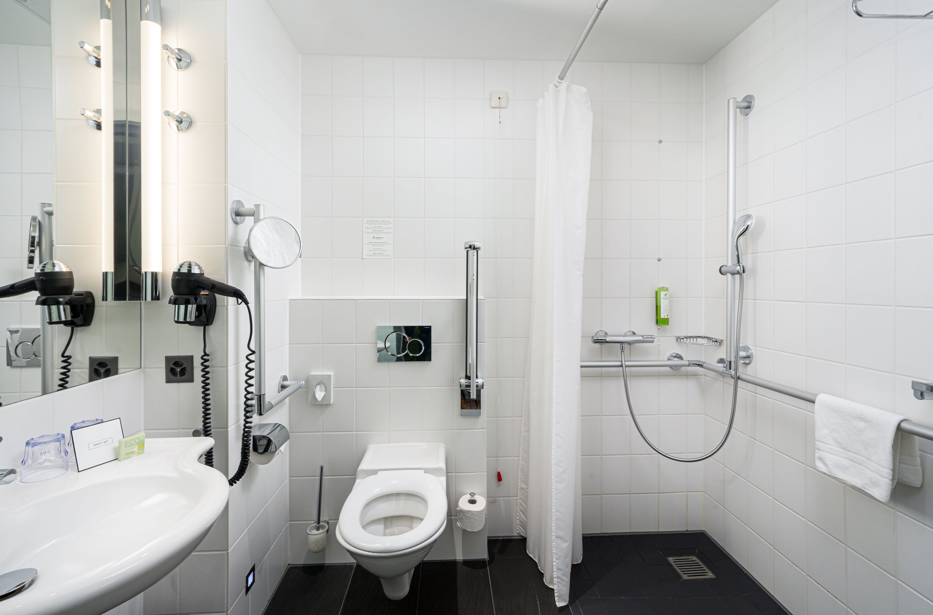 Un baño moderno con lavamanos, inodoro y zona de ducha blancos.