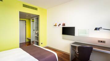 Une chambre d’hôtel comprenant un lit, un bureau, une chaise, une télévision et une porte donnant accès à une salle de bain.