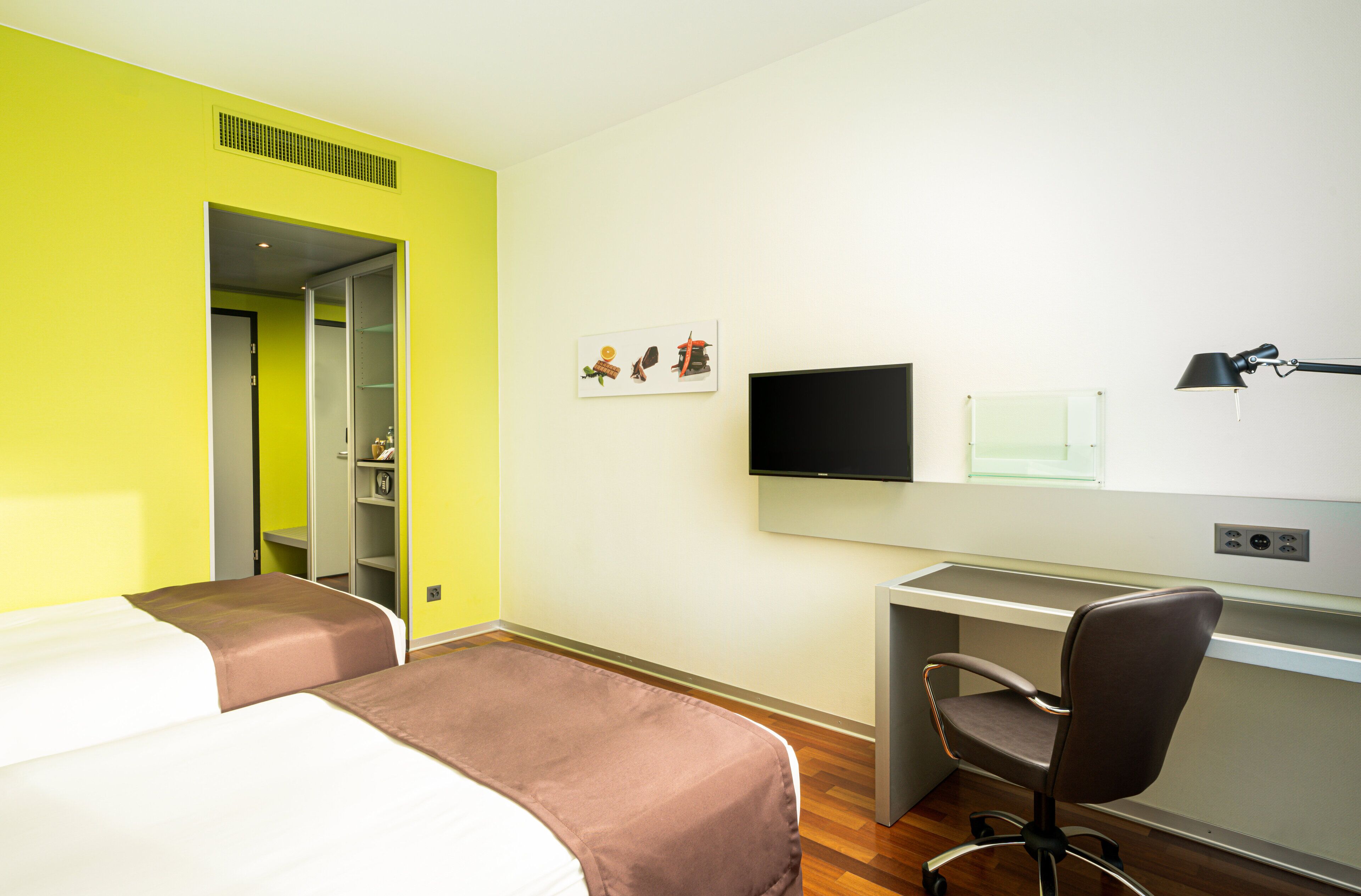 A hotel room with two beds, a desk, a chair, a television, and a window.