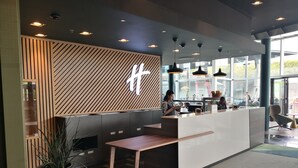 A modern reception area with a wooden panel design, a reception desk, and a large potted plant. - Holiday Inn BERN-WESTSIDE by IHG (Bern)