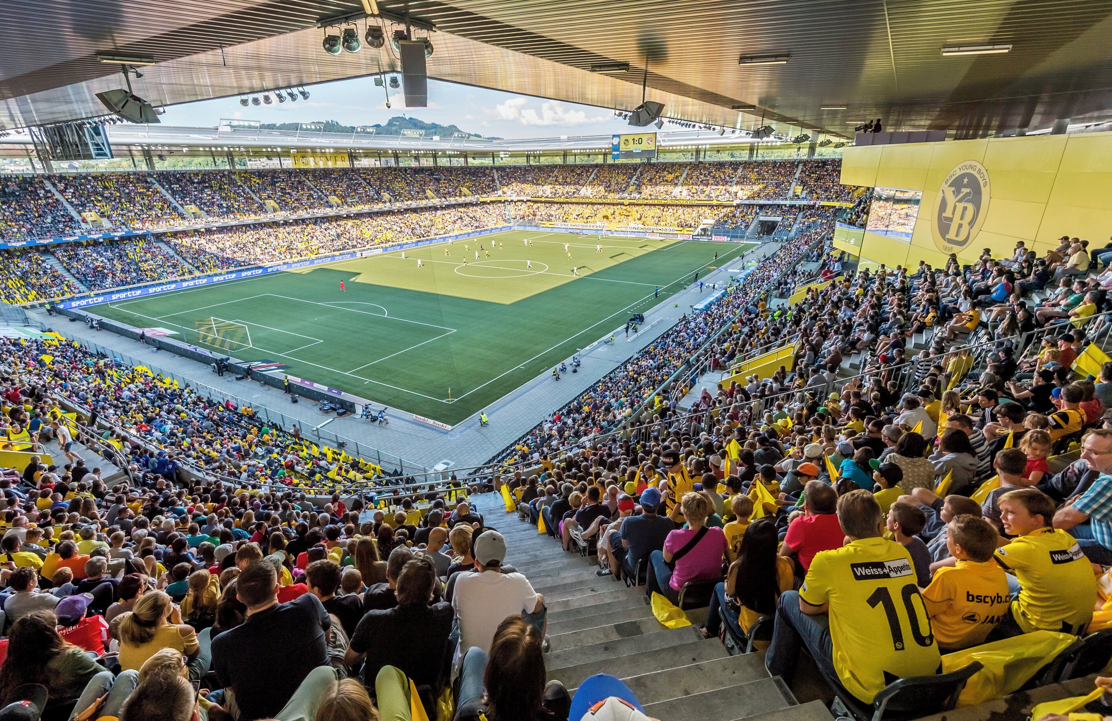 Ein Stadion voller Zuschauer mit Terrassenförmigen Sitzreihen und einem großen Spielfeld.