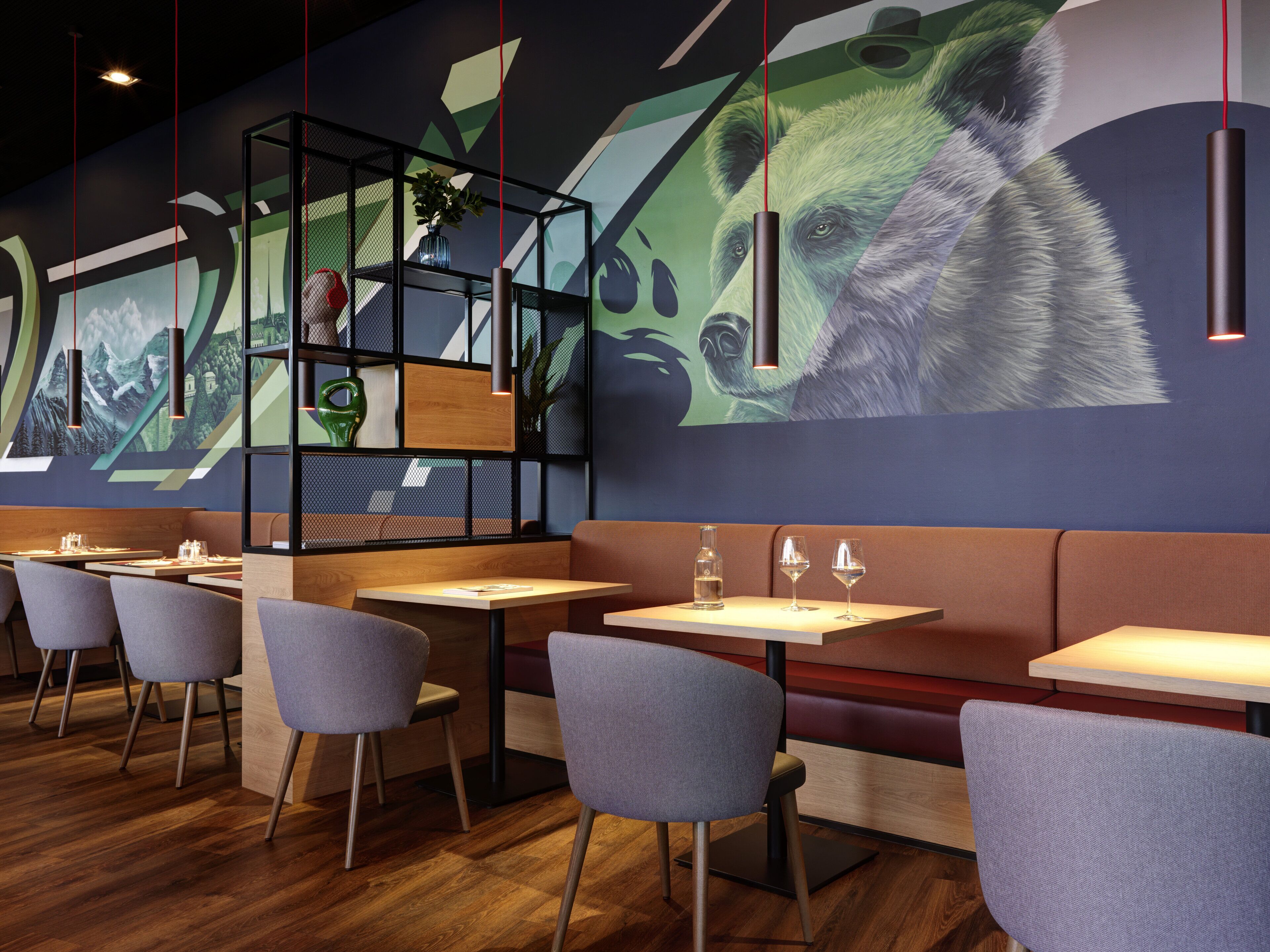 Un interior de restaurante moderno con mesas de madera, sillas tapizadas en gris y un gran mural de un oso en la pared.