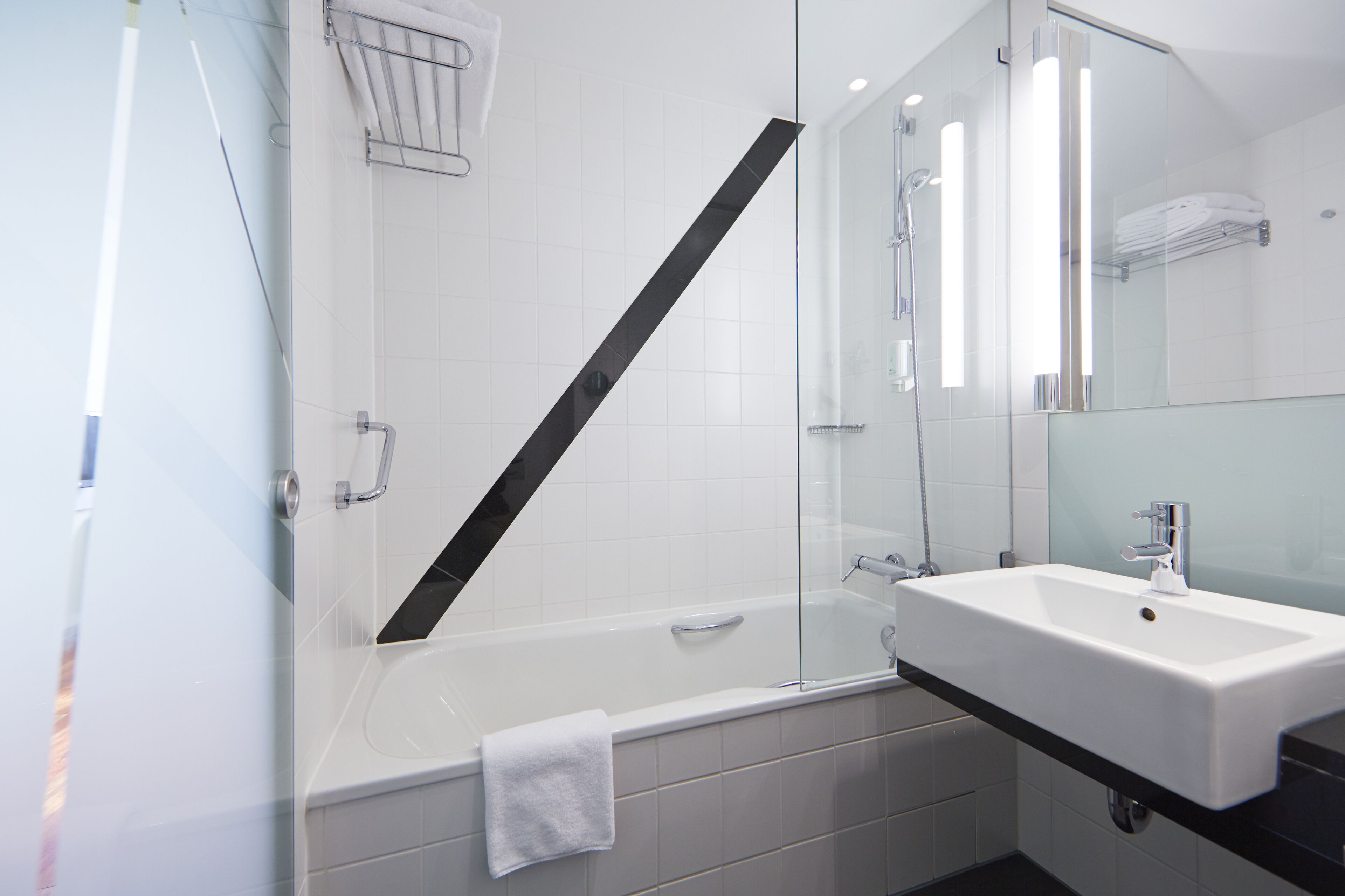 Un baño moderno con cabina de ducha de vidrio, una bañera blanca y un lavamanos con encimera negra.