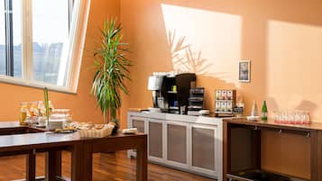 A hotel room with a dining area, a coffee station, a plant, and a view of the city.