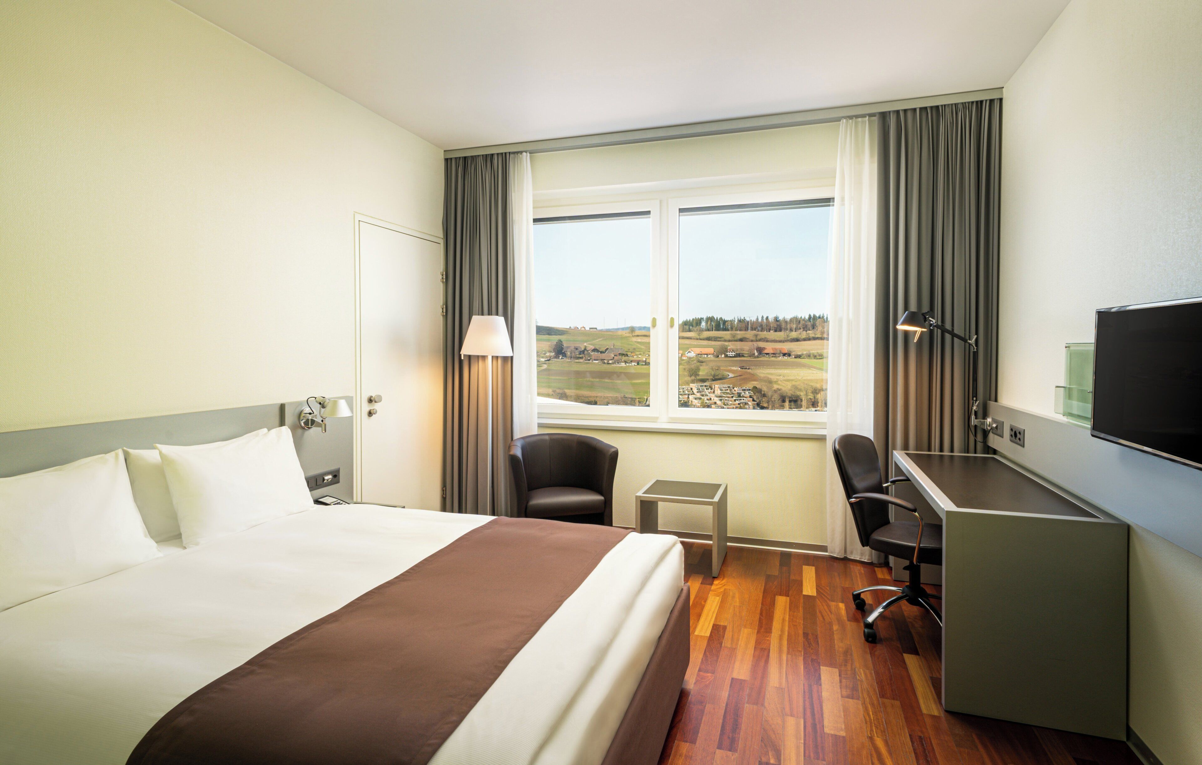 A hotel room with a bed, desk, chair, and a television.