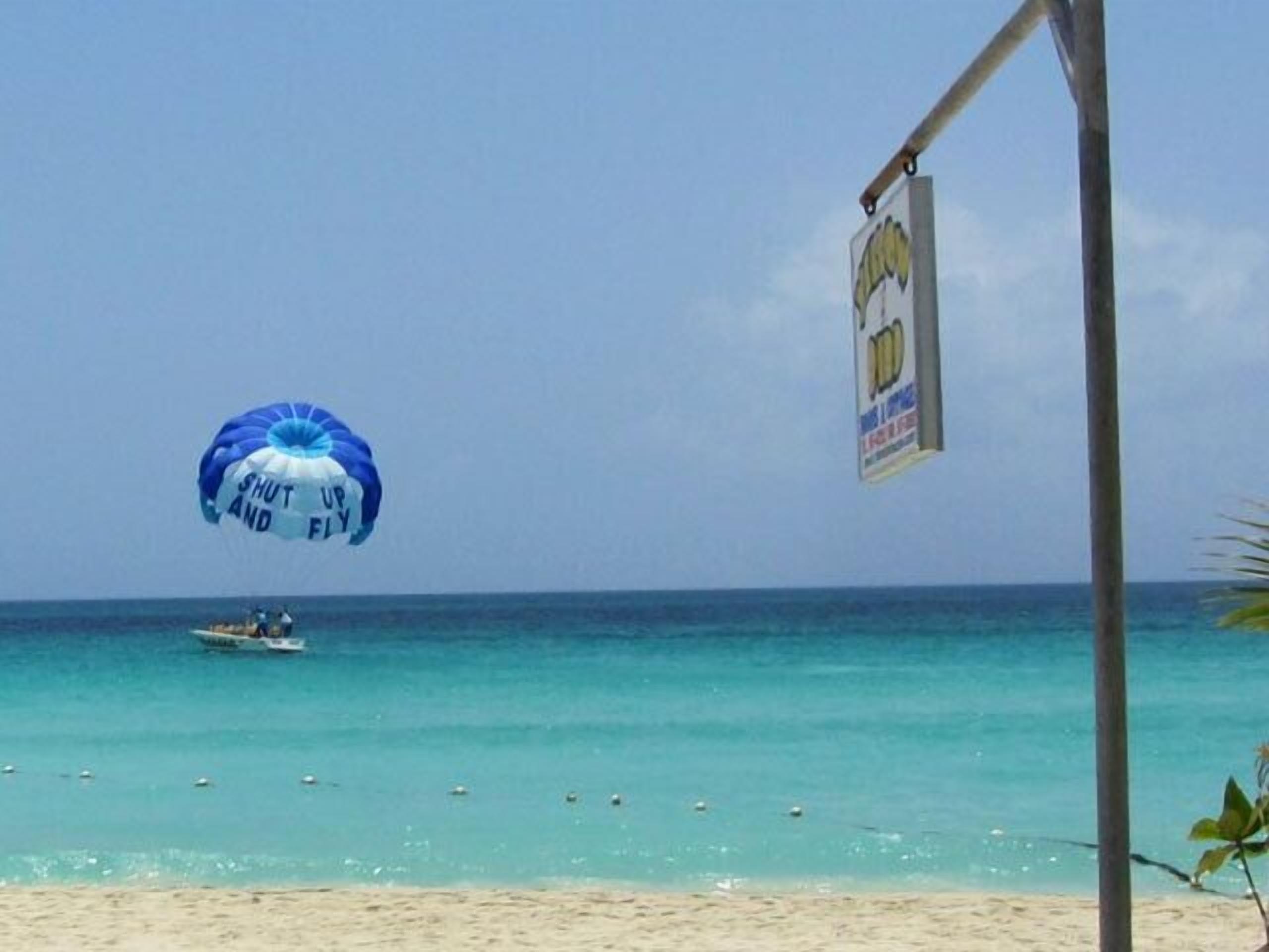 Una platja amb aigua turquesa cristal·lina, un vela de parascaig a l'aire i un vaixell a la distància.