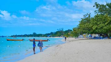 Ein Strand mit klarem, blauem Wasser, Booten und Menschen.