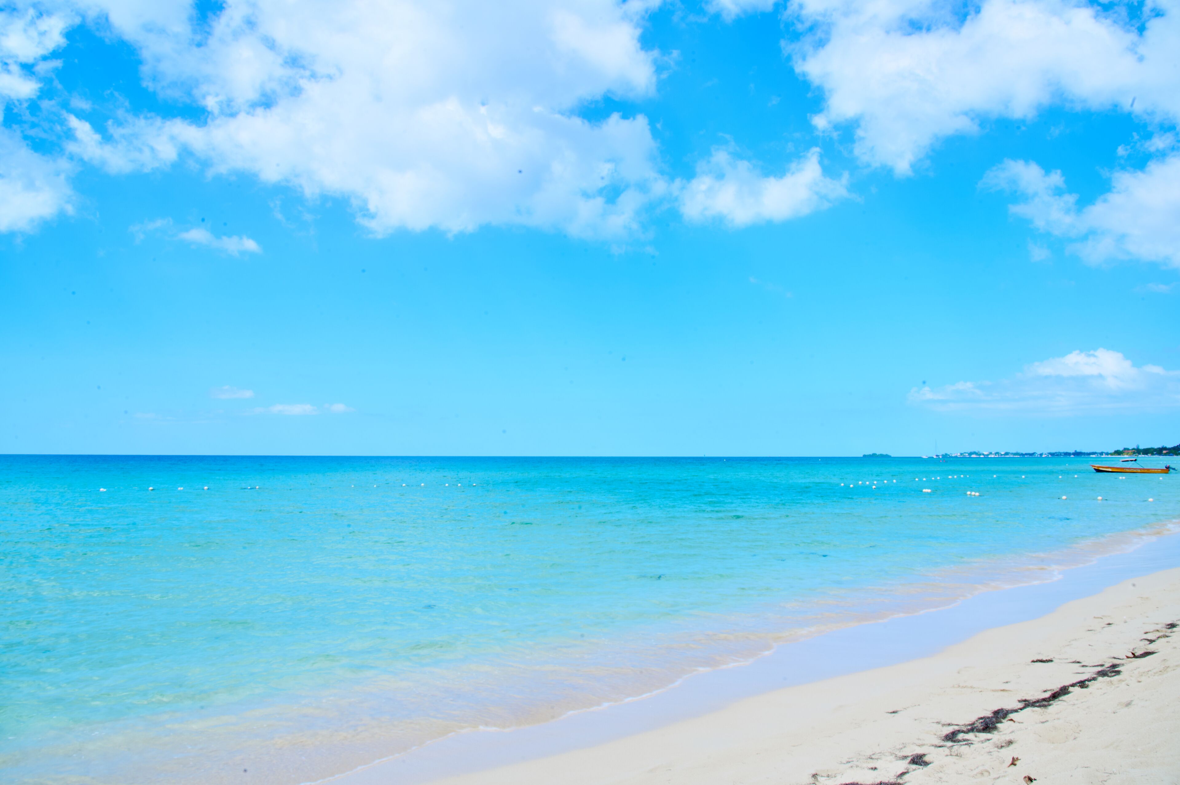 Ein Strand mit klarem, blauem Wasser, einem sandigen Ufer und einem Boot in der Ferne.