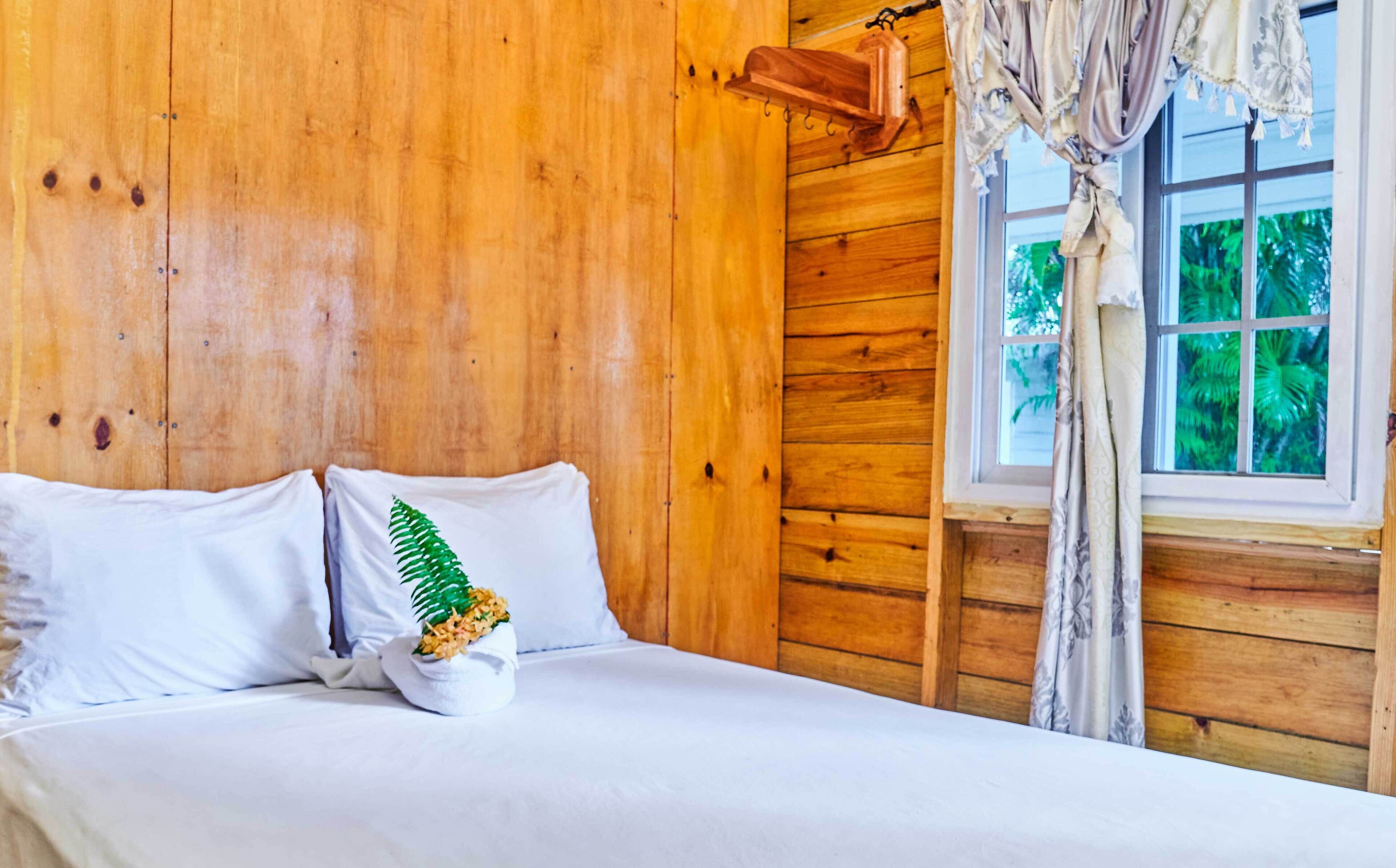 A wooden room with a bed, a window with curtains, and a hanging light fixture.