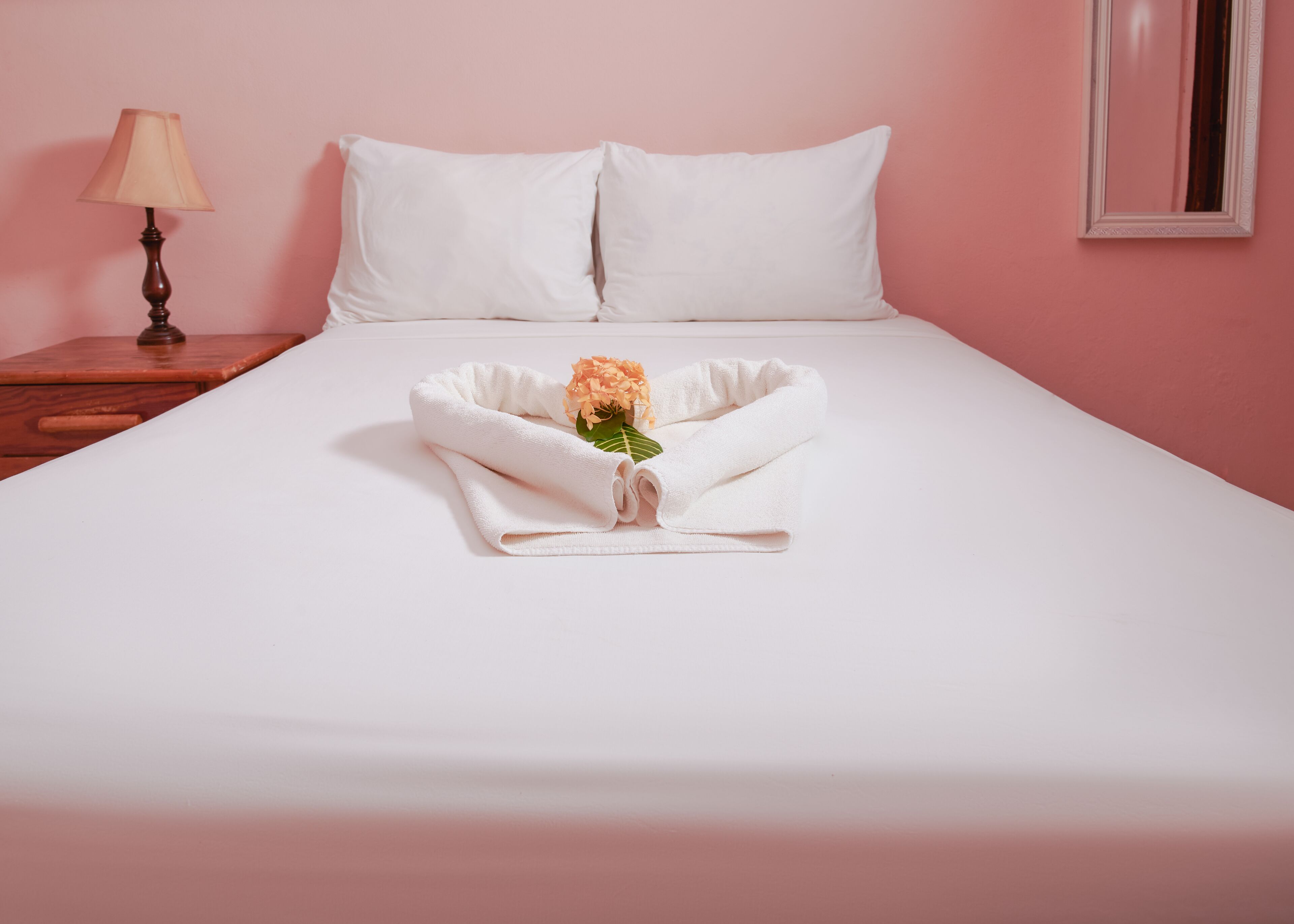 Un lit bien fait, avec des draps blancs, une serviette pliée et un petit bouquet de fleurs.
