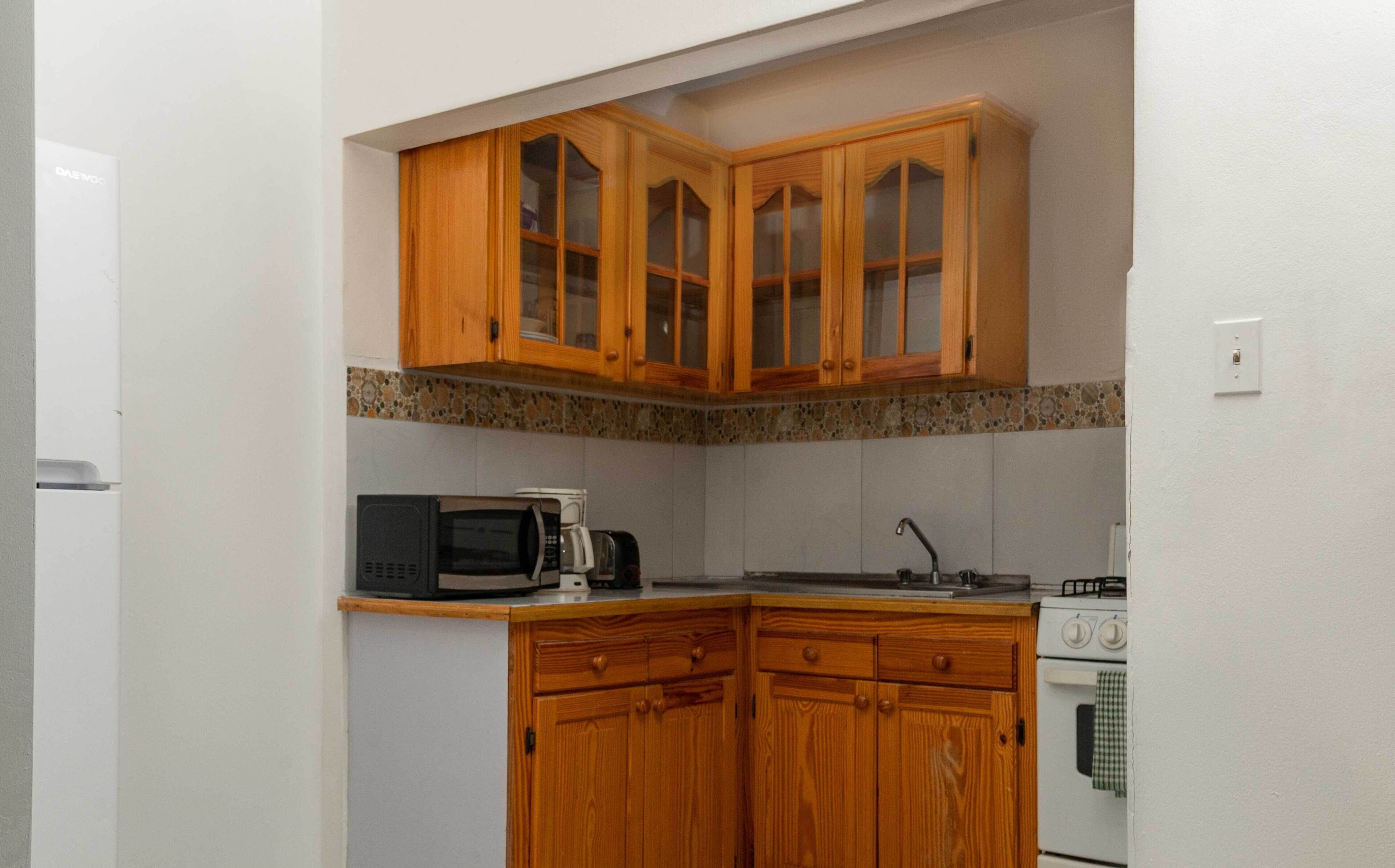 A compact kitchen with wooden cabinets, a microwave, a coffee maker, and a stove.