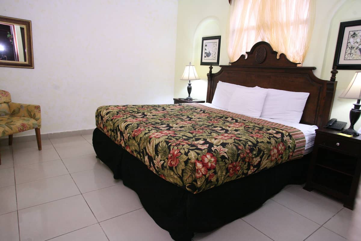 A neatly made bed with a floral bedspread, a wooden headboard, and a bedside table with a lamp.