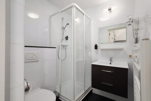 A modern bathroom with a glass-enclosed shower, a white sink, and a dark-toned vanity. - Hotel Light (Rotterdam)