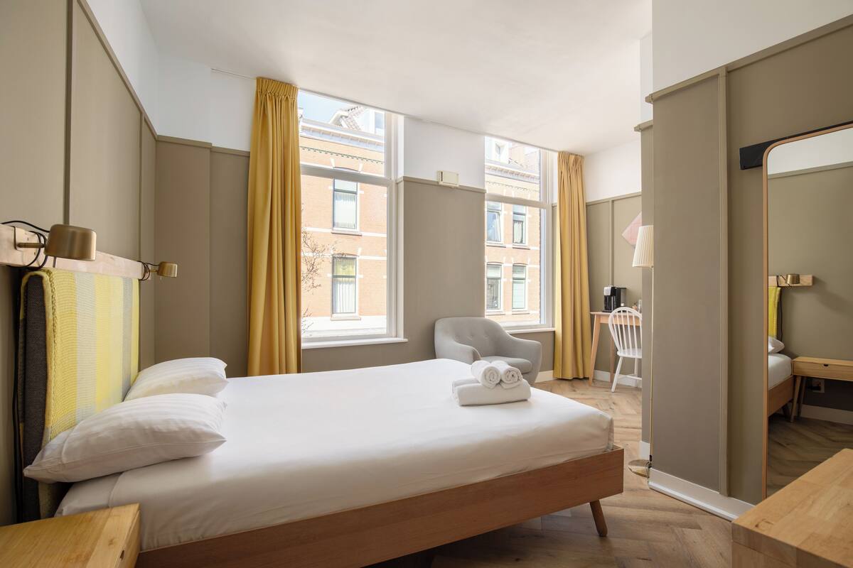 A hotel room with a large bed, a desk, a chair, and a mirror.