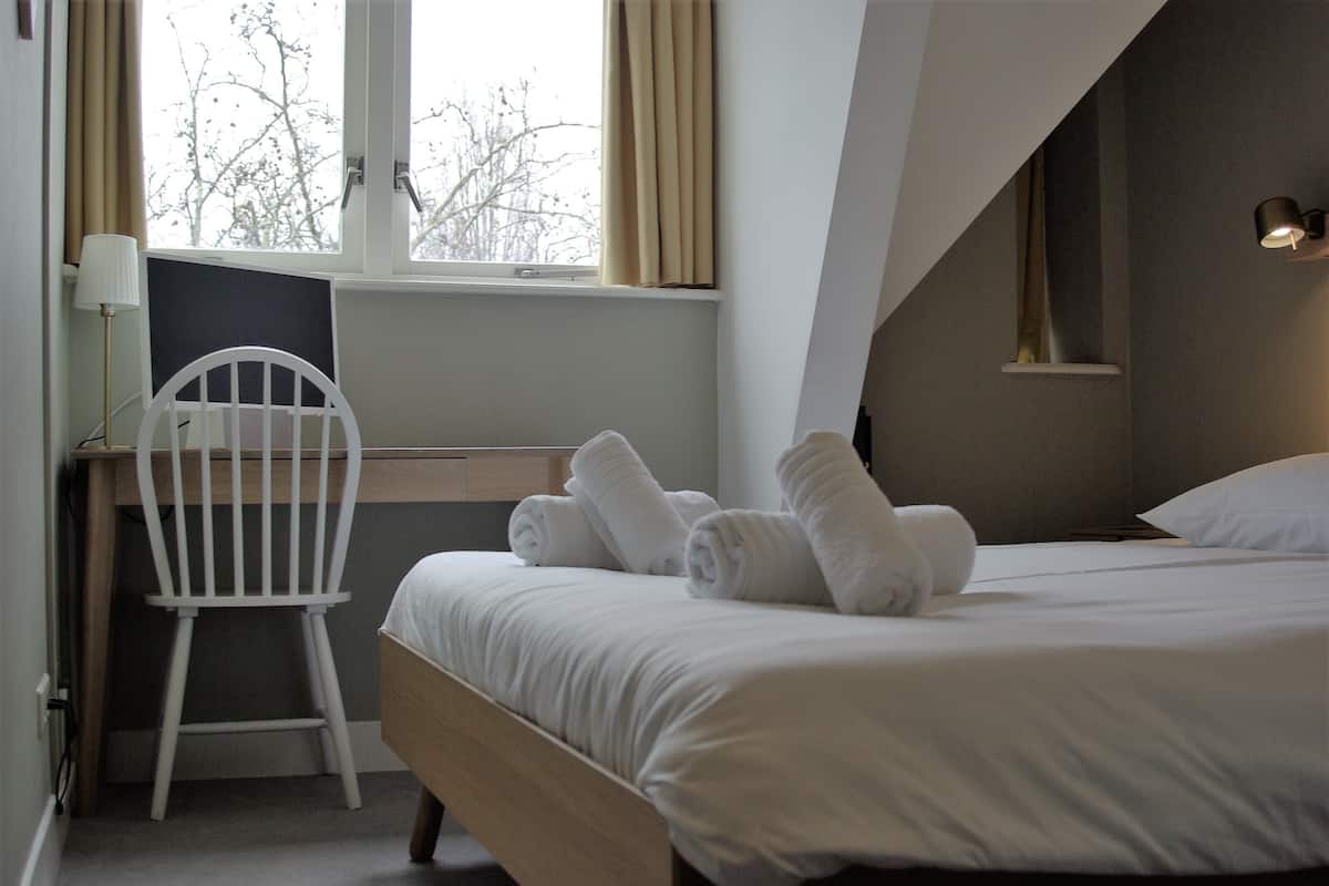 A hotel room with a bed, a desk, a chair, and a window with curtains.