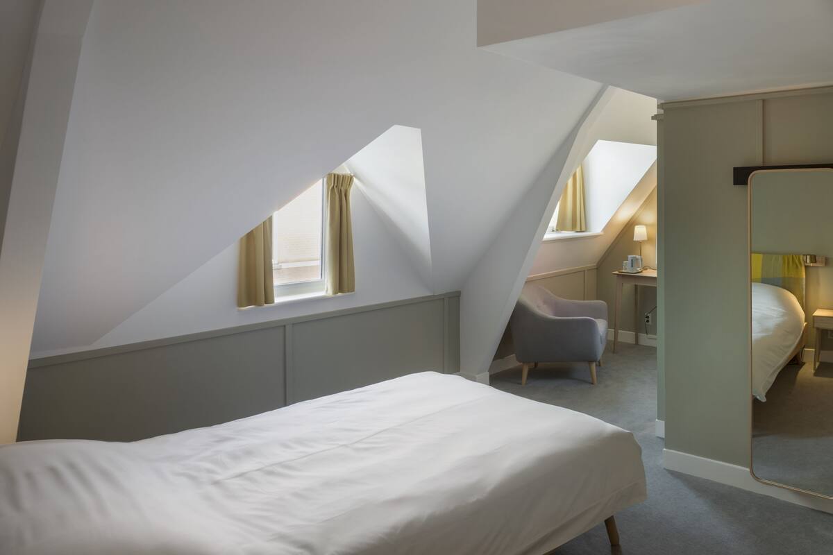 A bedroom with a bed, a chair, a desk, and a mirror.