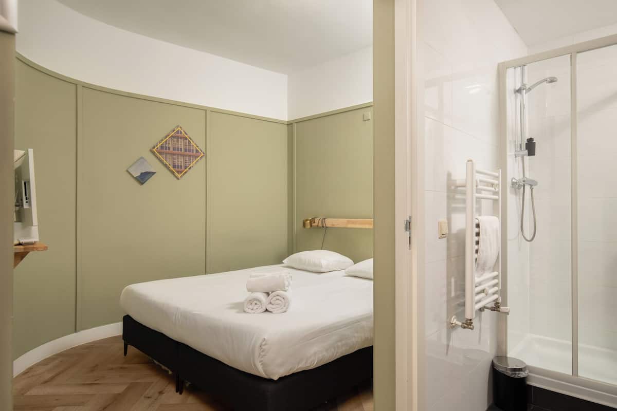 A hotel room with a bed, a shower, and a small shelf with a towel.