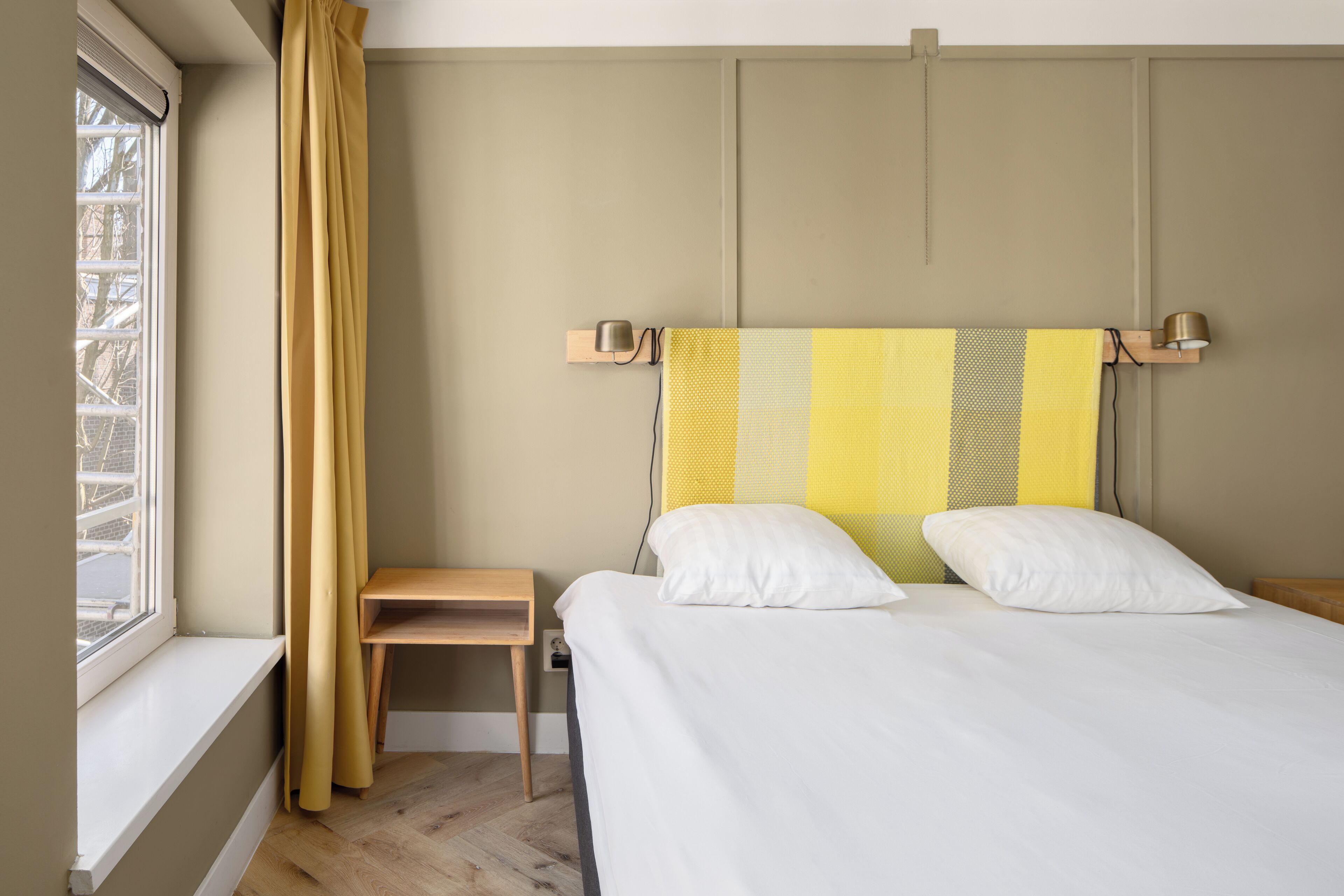 A bedroom with a bed, a nightstand, a lamp, and a window with curtains.