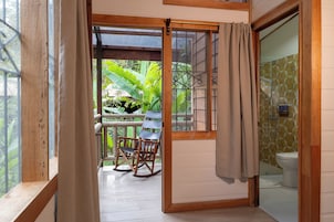 Habitación con estructura de madera que ofrece vistas a vegetación exuberante, una mecedora y un inodoro con un revestimiento de pared estampado.