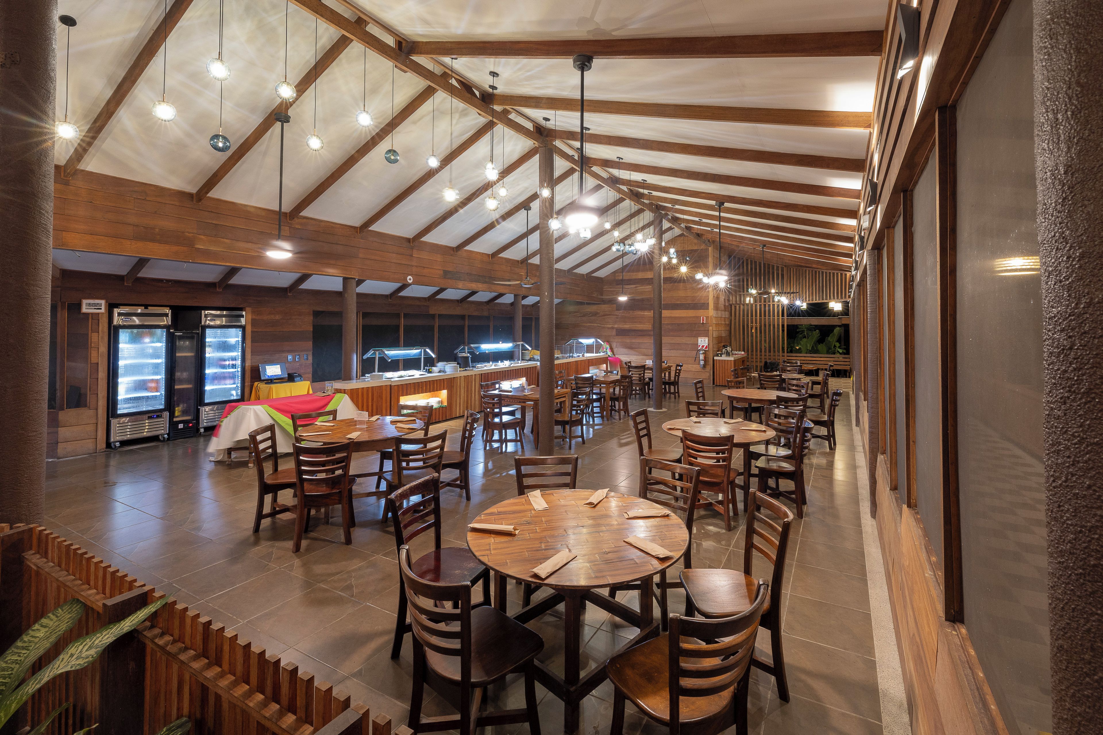 En rummelig restaurant med høje lofter og træbjælker, med flere spiseborde og stole.