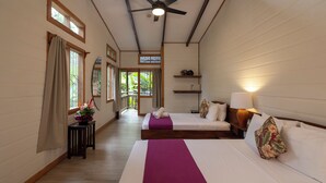 Una habitación de hotel con dos camas, un ventilador de techo, una ventana con cortinas, una mesita con un jarrón y vistas al exterior.
