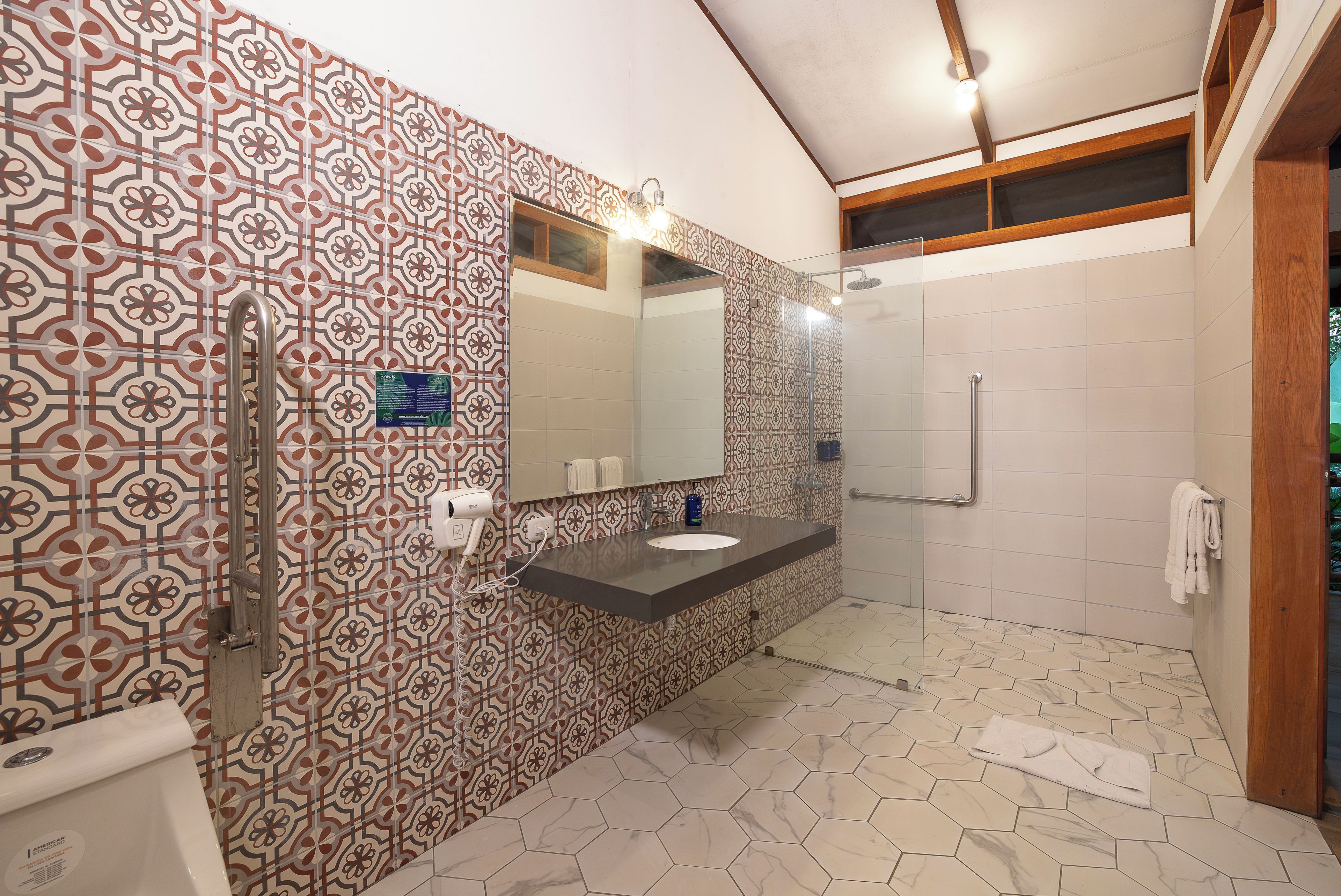 Un baño con pared de baldosas estampadas, cabina de ducha de cristal y tocador con espejo.