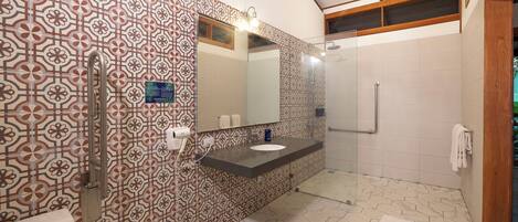 Un baño con pared de baldosas estampadas, cabina de ducha de cristal y tocador con espejo.