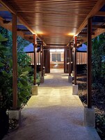 Un corredor cubierto con techo de madera y pilares de concreto, que conduce a un edificio con el letrero 'Pachira Lodge'.