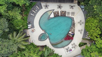 An aerial view of a resort with a large swimming pool, sun loungers, and surrounding greenery.