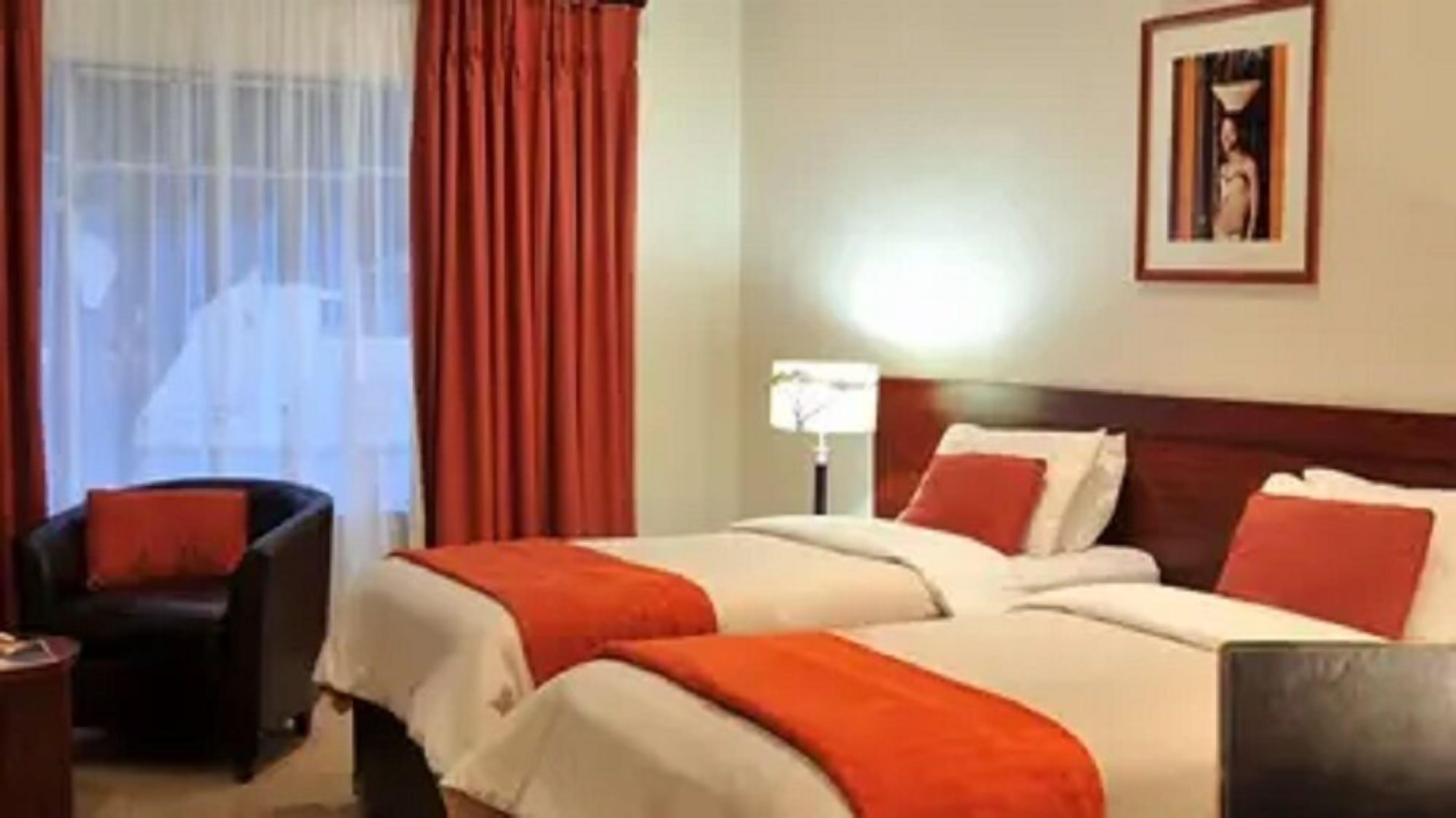 A hotel room with two beds, a chair, a lamp, and a framed picture on the wall.