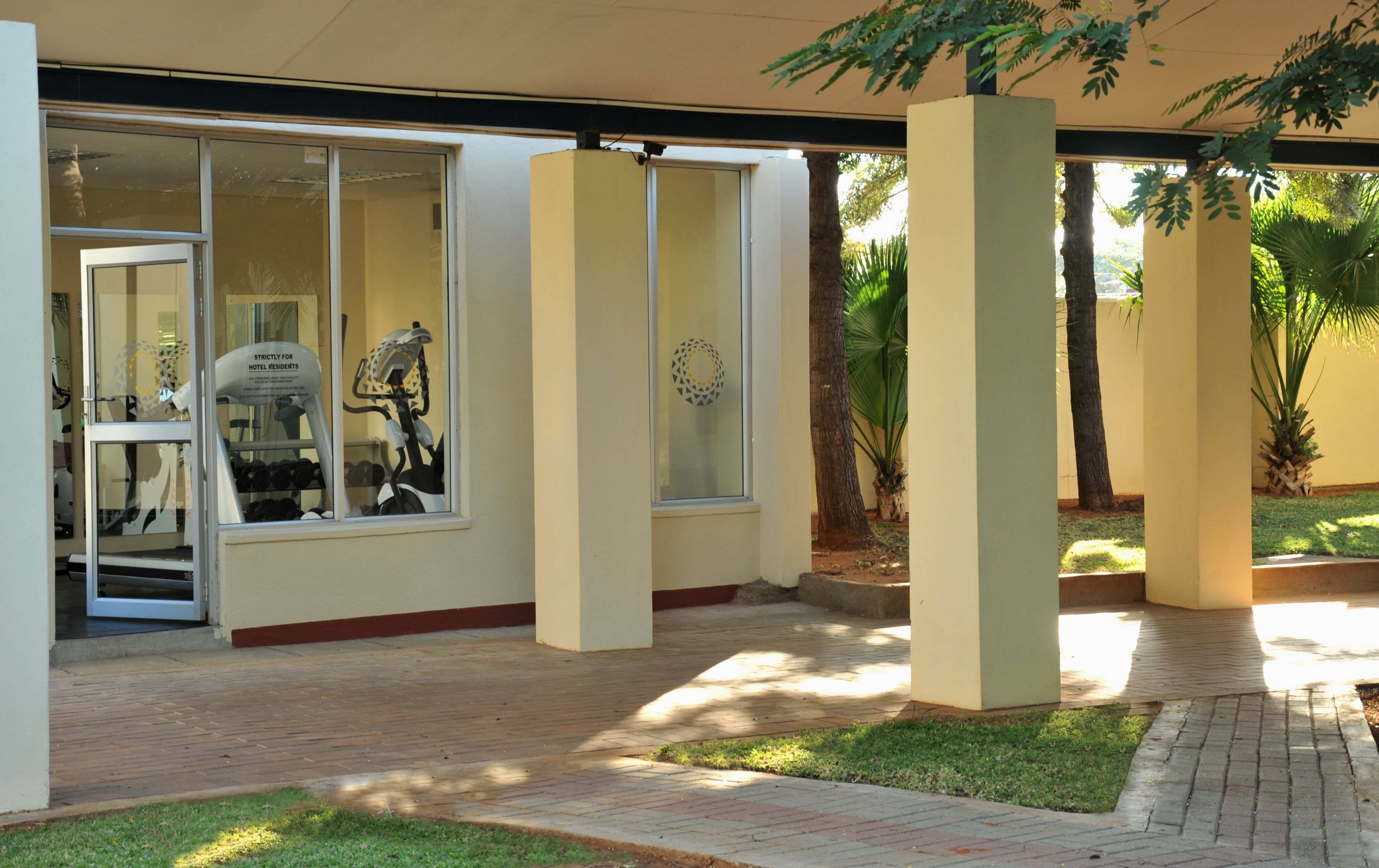 A hotel entrance with a glass door, a bicycle parked inside, and a palm tree in the background.