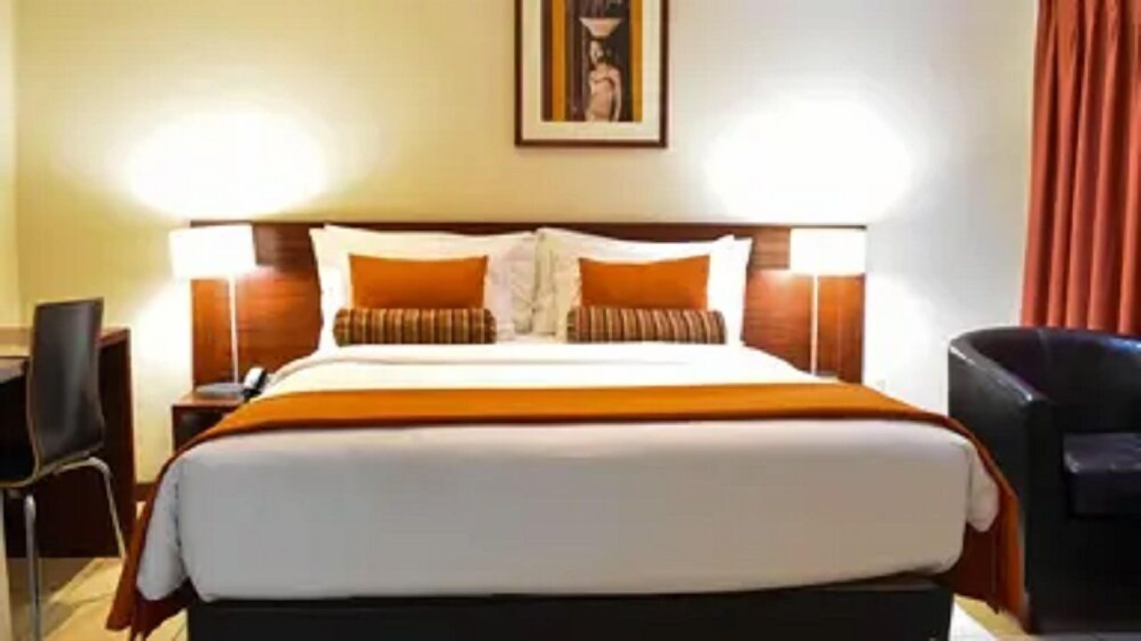 A hotel room with a large bed, two bedside tables, a chair, and a painting on the wall.
