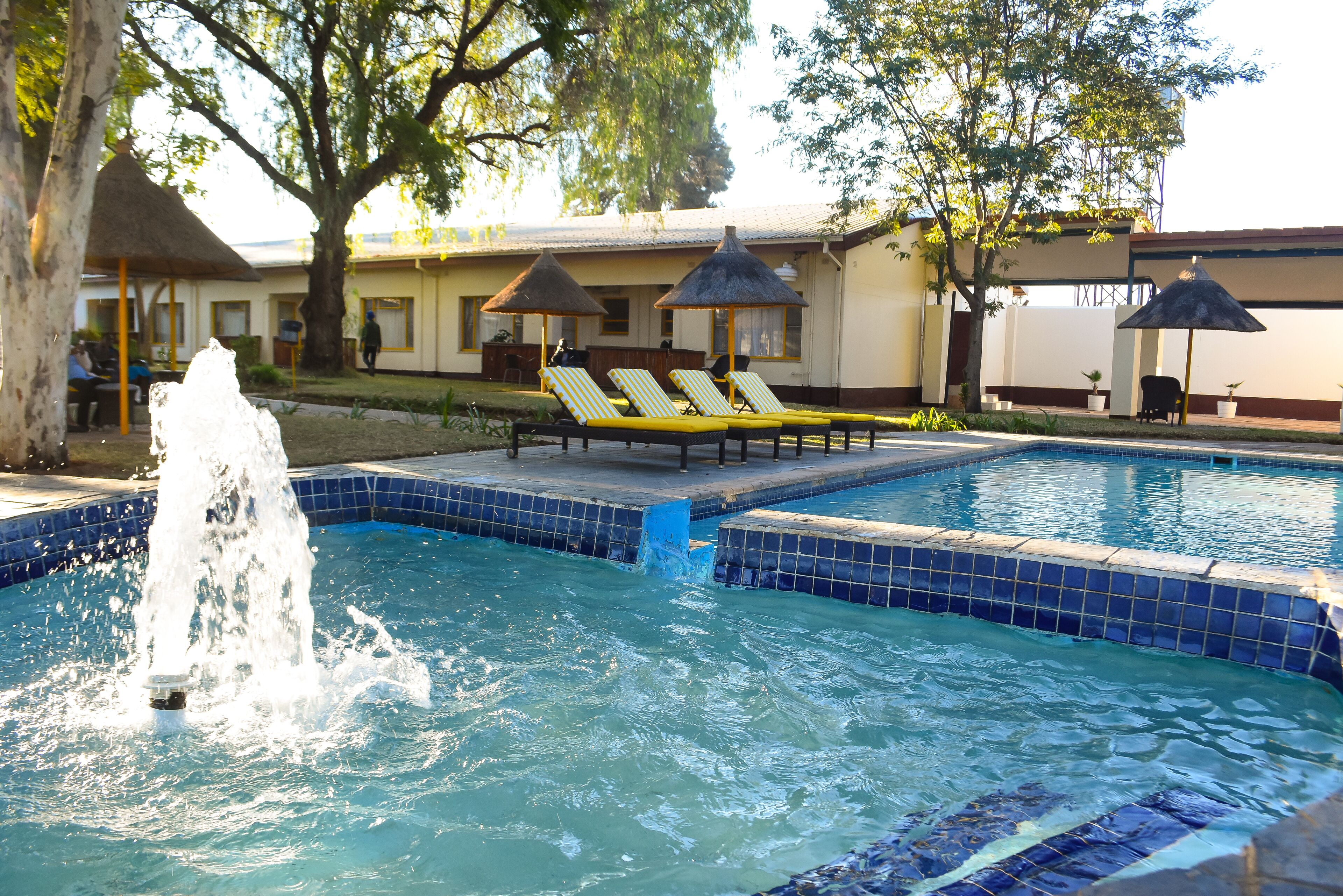 A swimming pool with a water fountain, lounge chairs, and umbrellas.