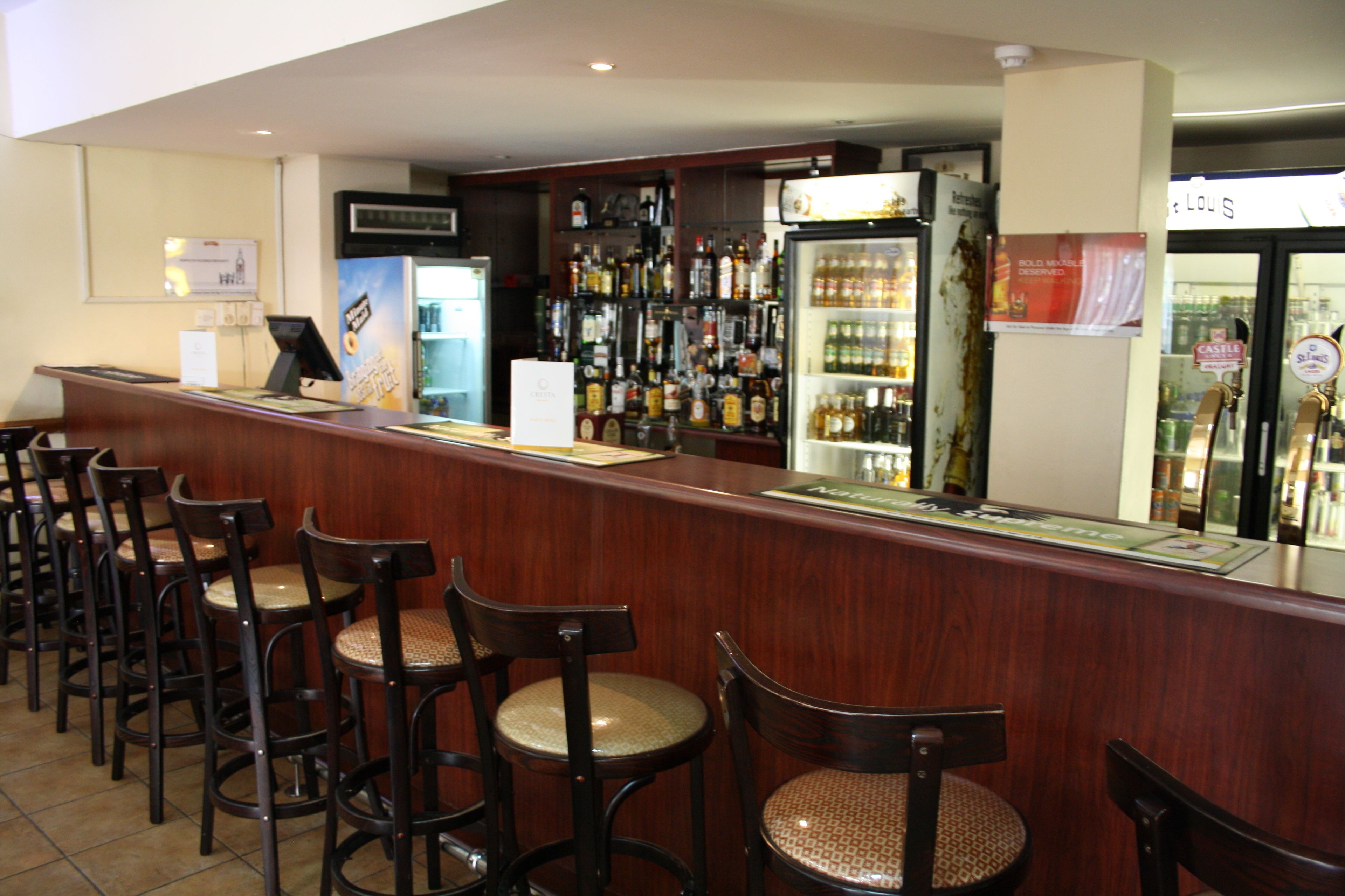 A bar area with a wooden counter, several bar stools, and a refrigerator stocked with beverages.
