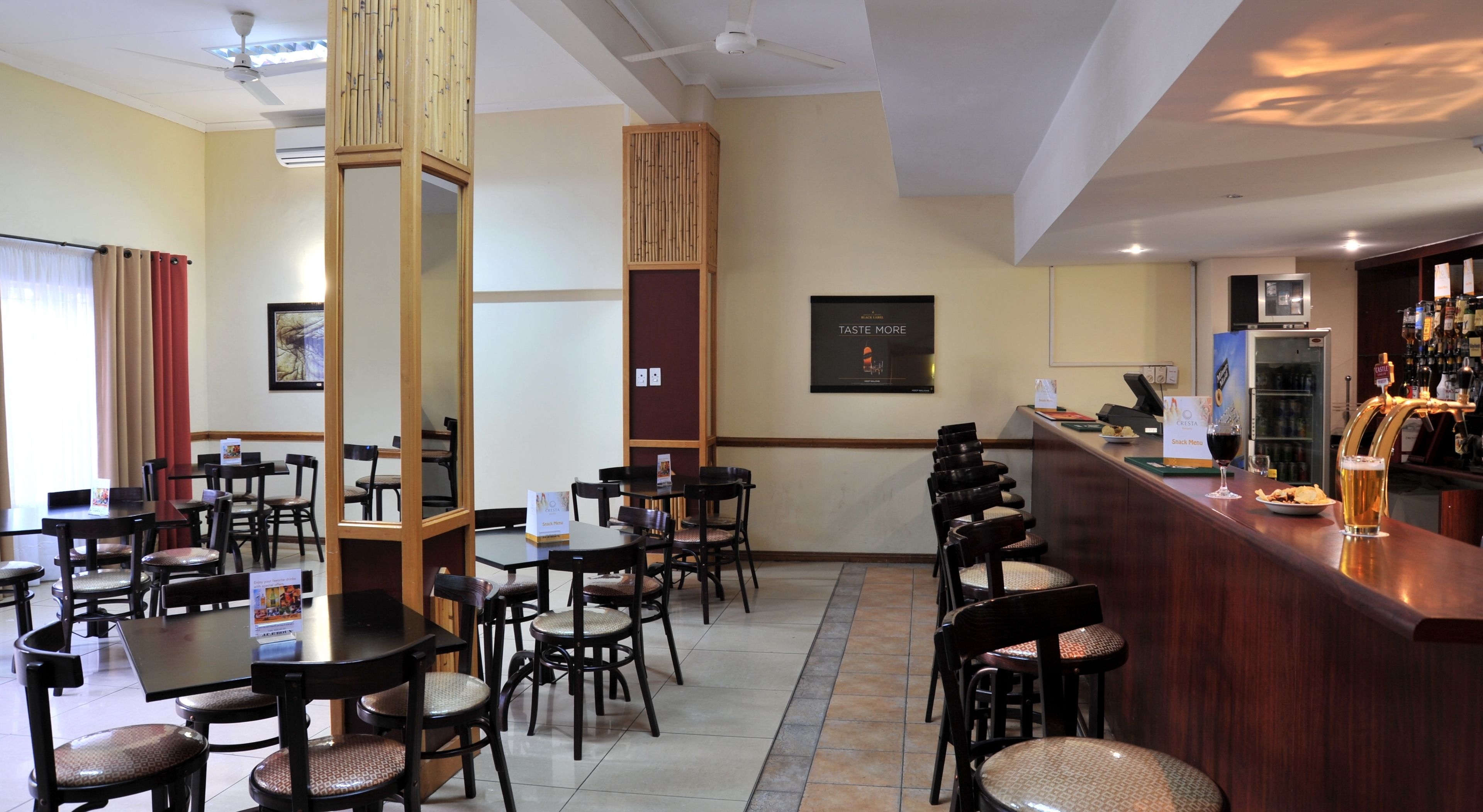 Un restaurante con varias mesas y sillas, una zona de bar con mostrador y taburetes, y un tablero de menú colgado en la pared.
