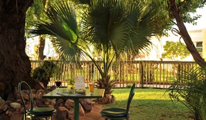 An outdoor seating area with a table and chairs, surrounded by rocks and greenery, including a palm tree.