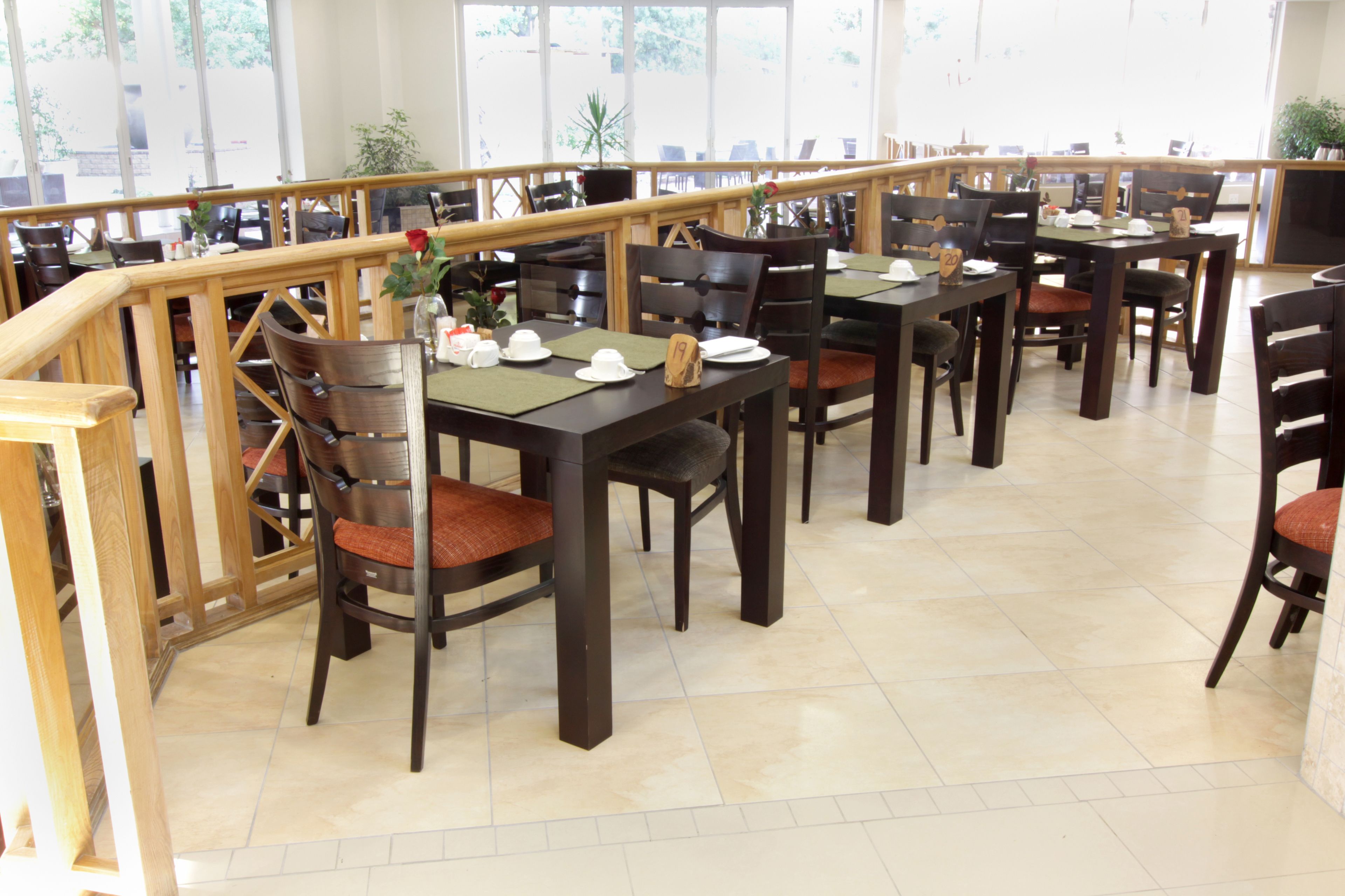 A spacious dining area with multiple tables and chairs, wooden railings, and large windows allowing natural light.