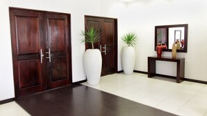 A hallway with wooden doors, a tiled floor, and a console table with a mirror and decorative items. - Cresta Lodge Gaborone (Gaborone)