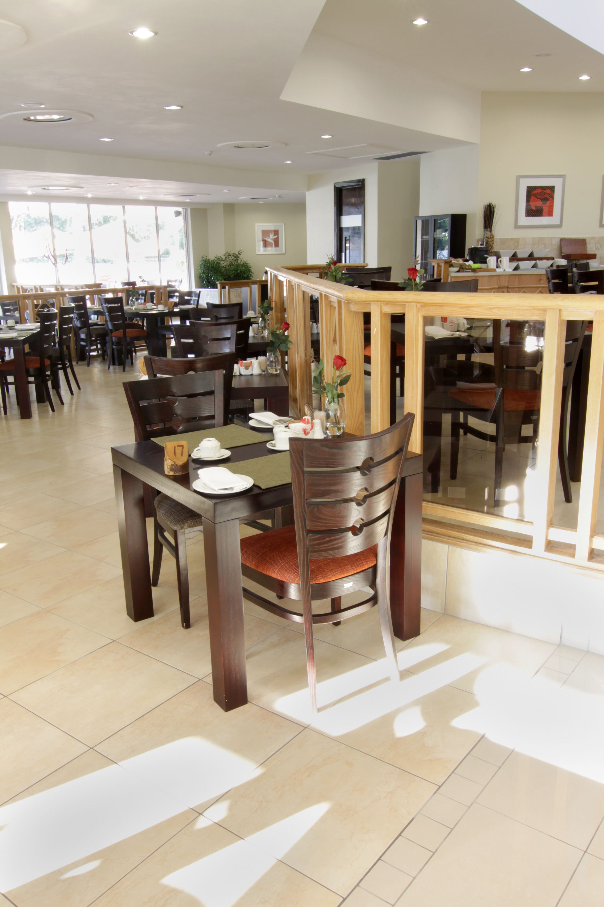 A spacious dining area with multiple tables and chairs, a counter with a cash register, and a large window providing natural light.