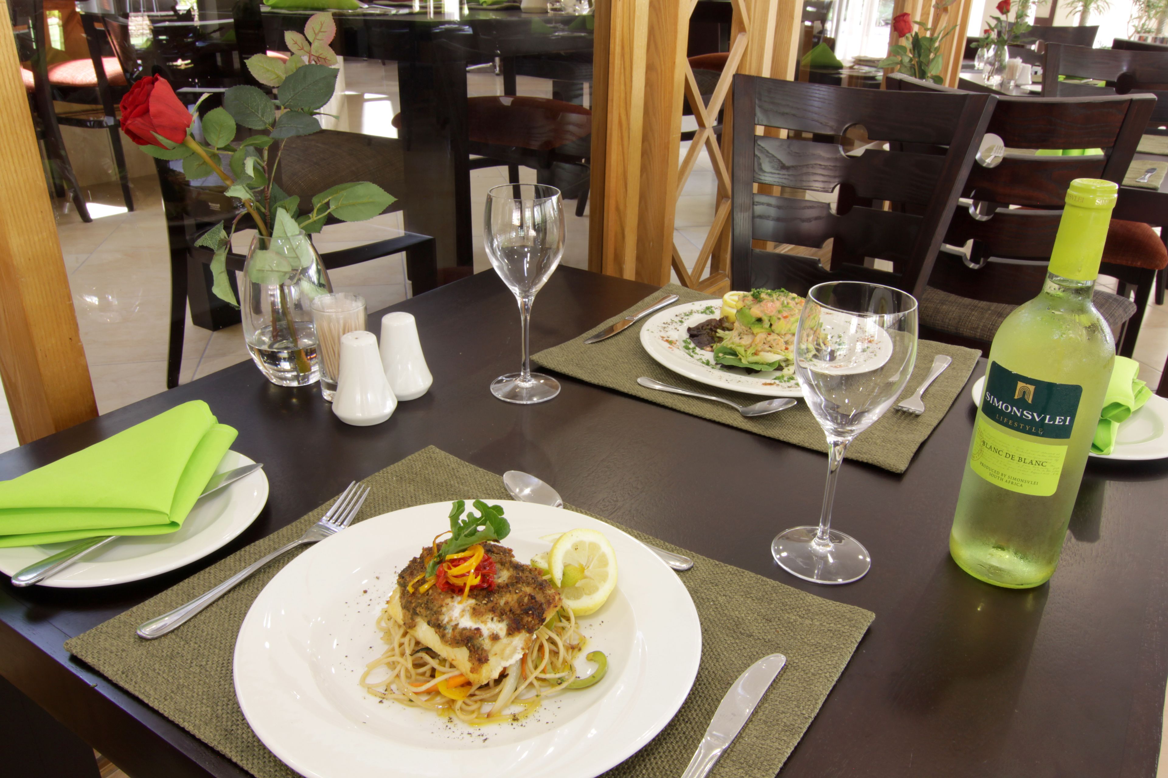 A dining table with a plate of food, a wine glass, and a bottle of wine.