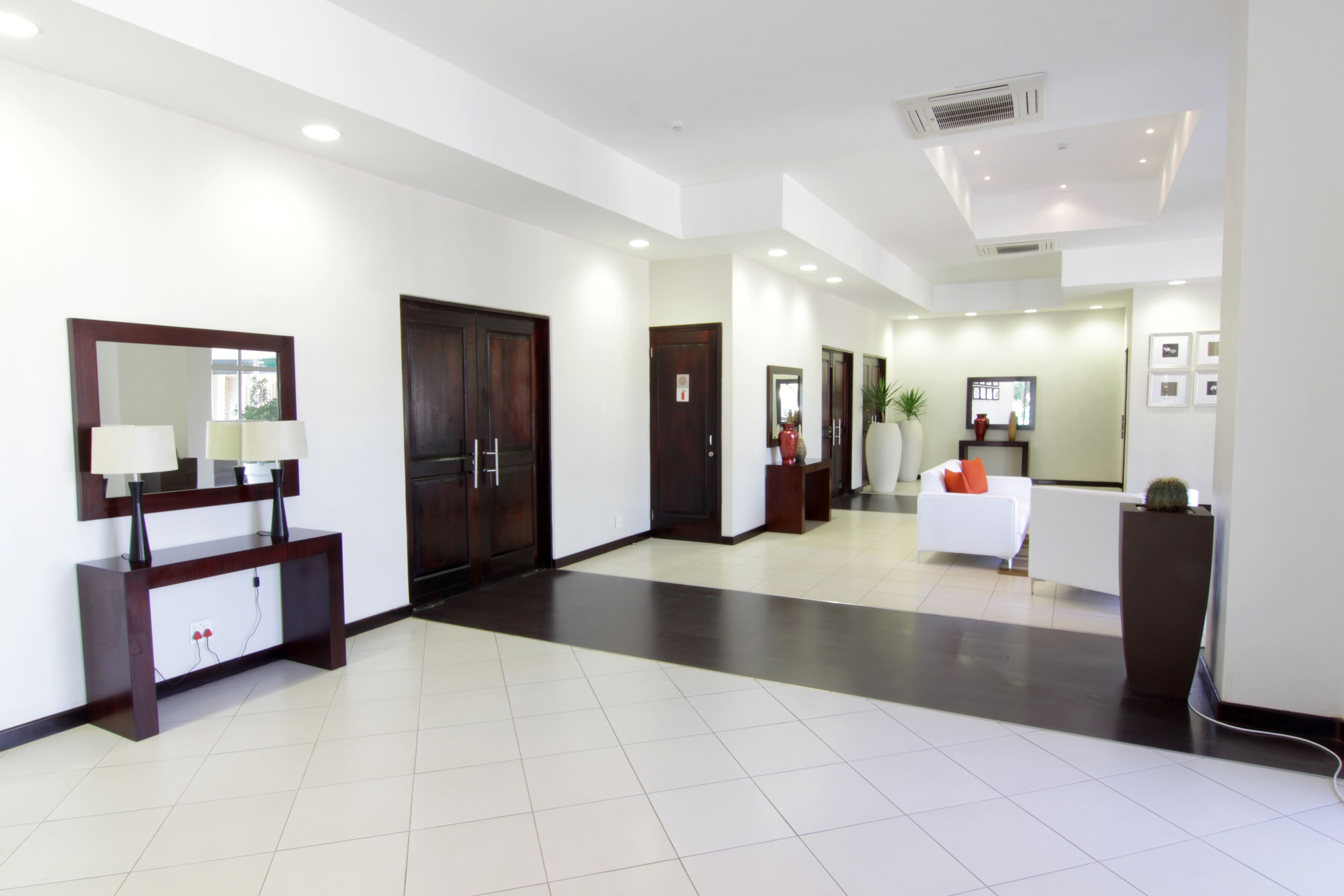 Un moderno vestíbulo de hotel con mostrador de recepción, un espejo grande y una zona de estar con sofá blanco.
