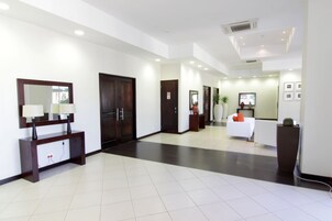 Un moderno vestíbulo de hotel con mostrador de recepción, un espejo grande y una zona de estar con sofá blanco.