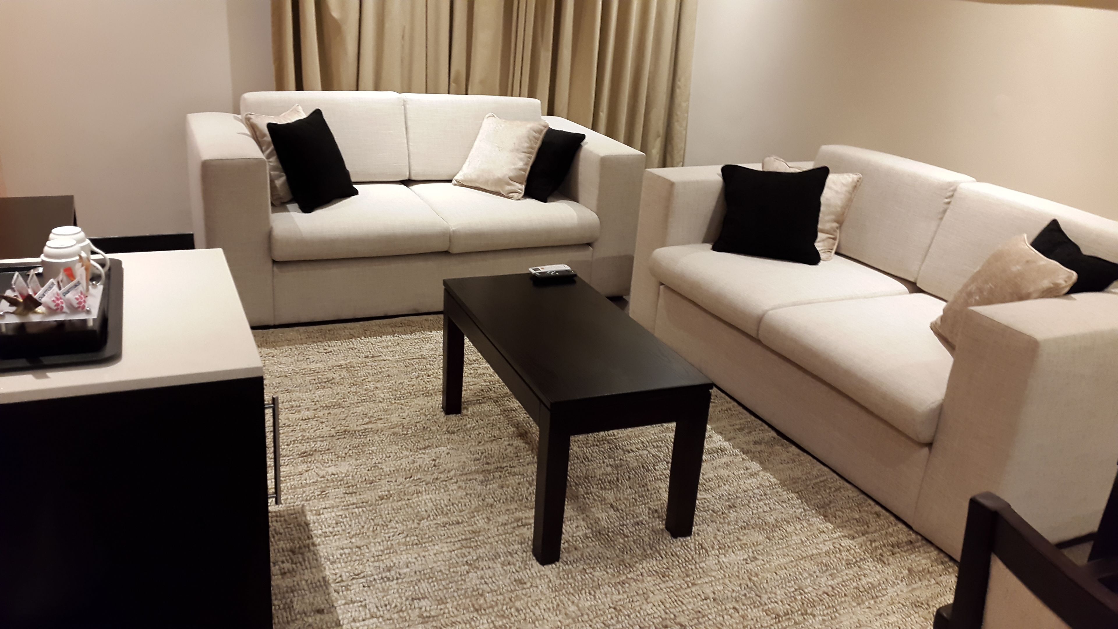 A modern living room with two white sofas, a black coffee table, and a small side table with a tray of items.