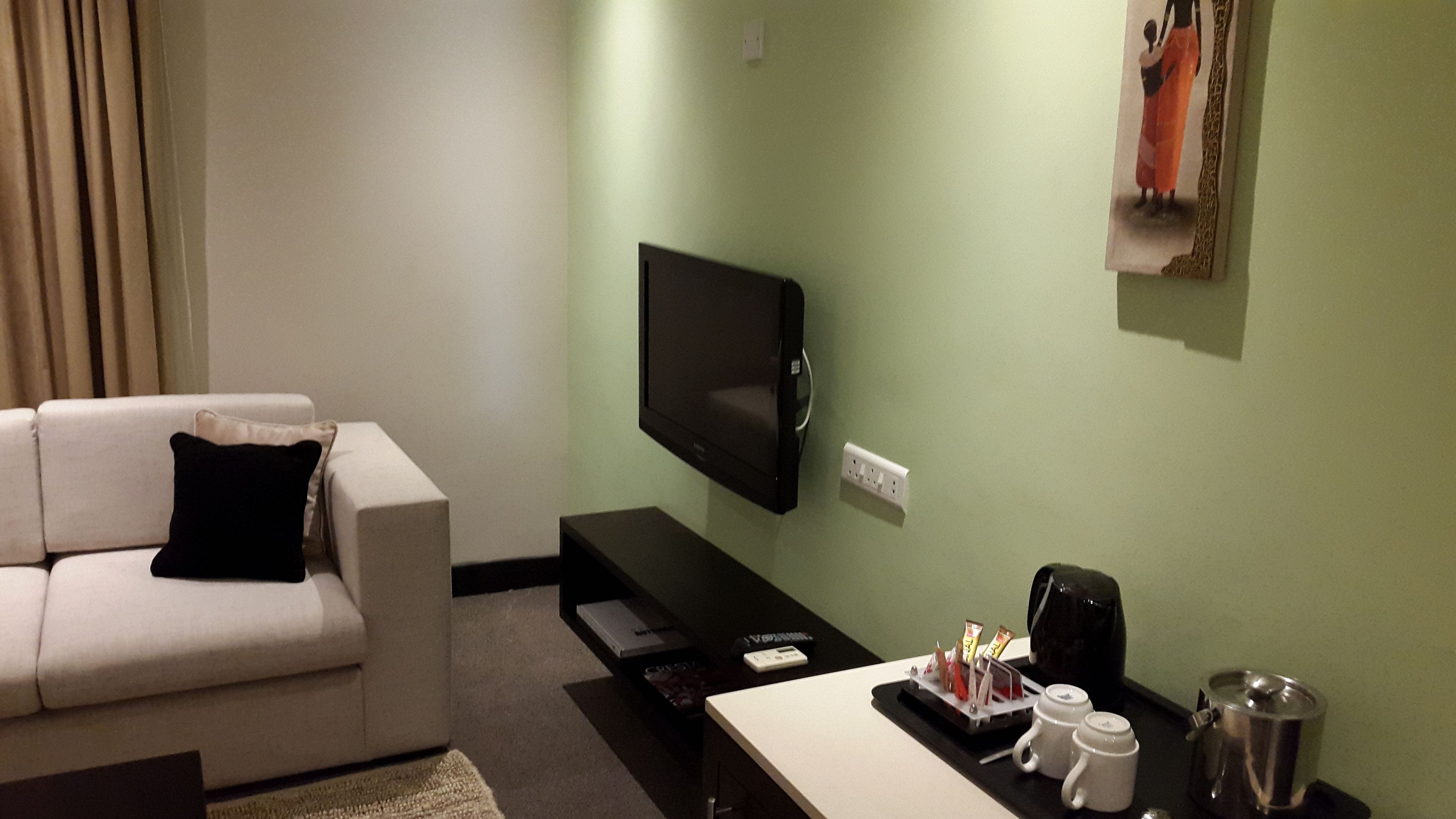 A modern living room with a flat-screen TV mounted on the wall, a sofa, a coffee table, and a tray with cups and a pot.