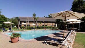 A pool area with lounge chairs and umbrellas, surrounded by a brick patio and greenery. - Cresta Lodge Gaborone (Gaborone)