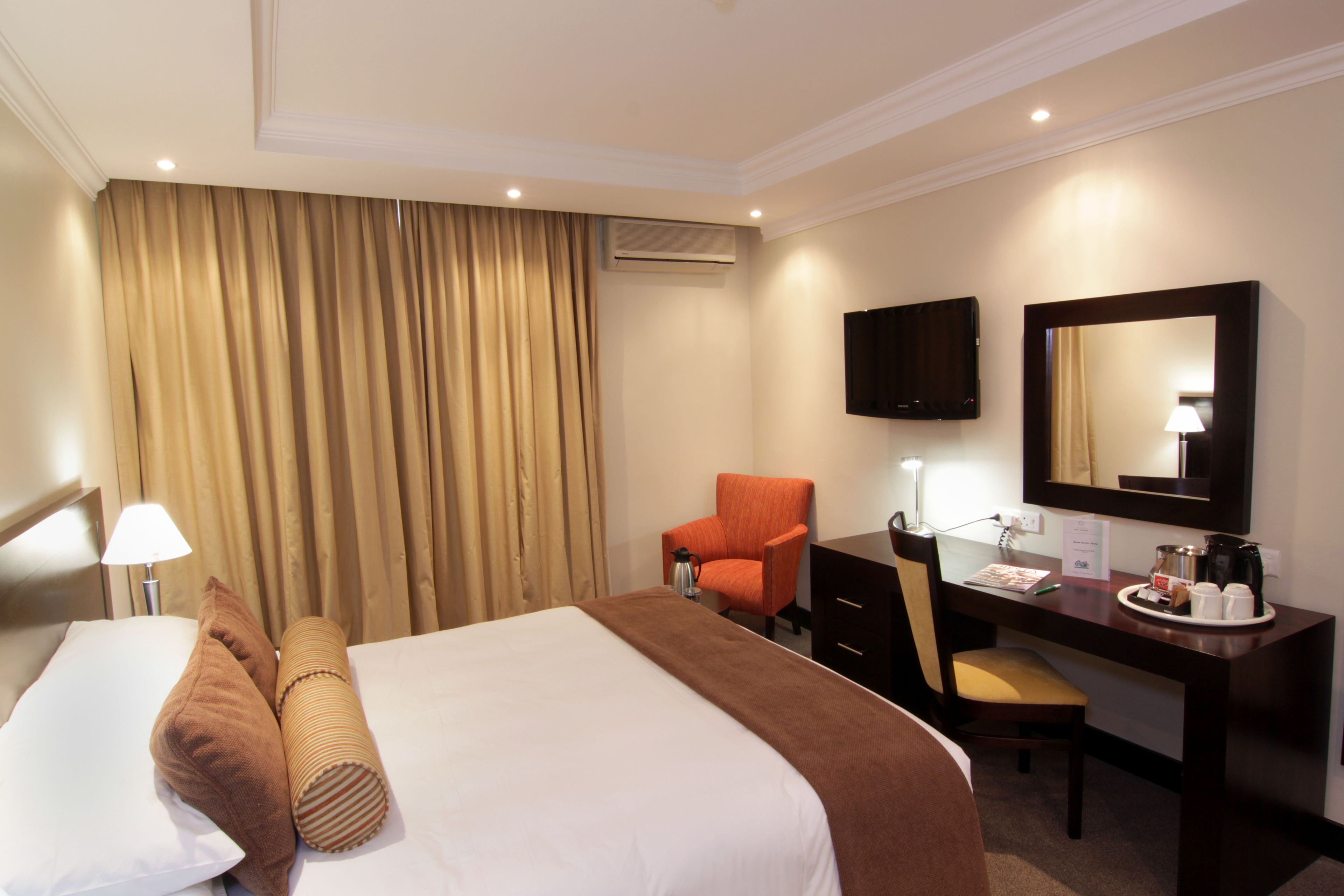 A hotel room with a bed, a desk, a chair, a television, and an air conditioning unit.