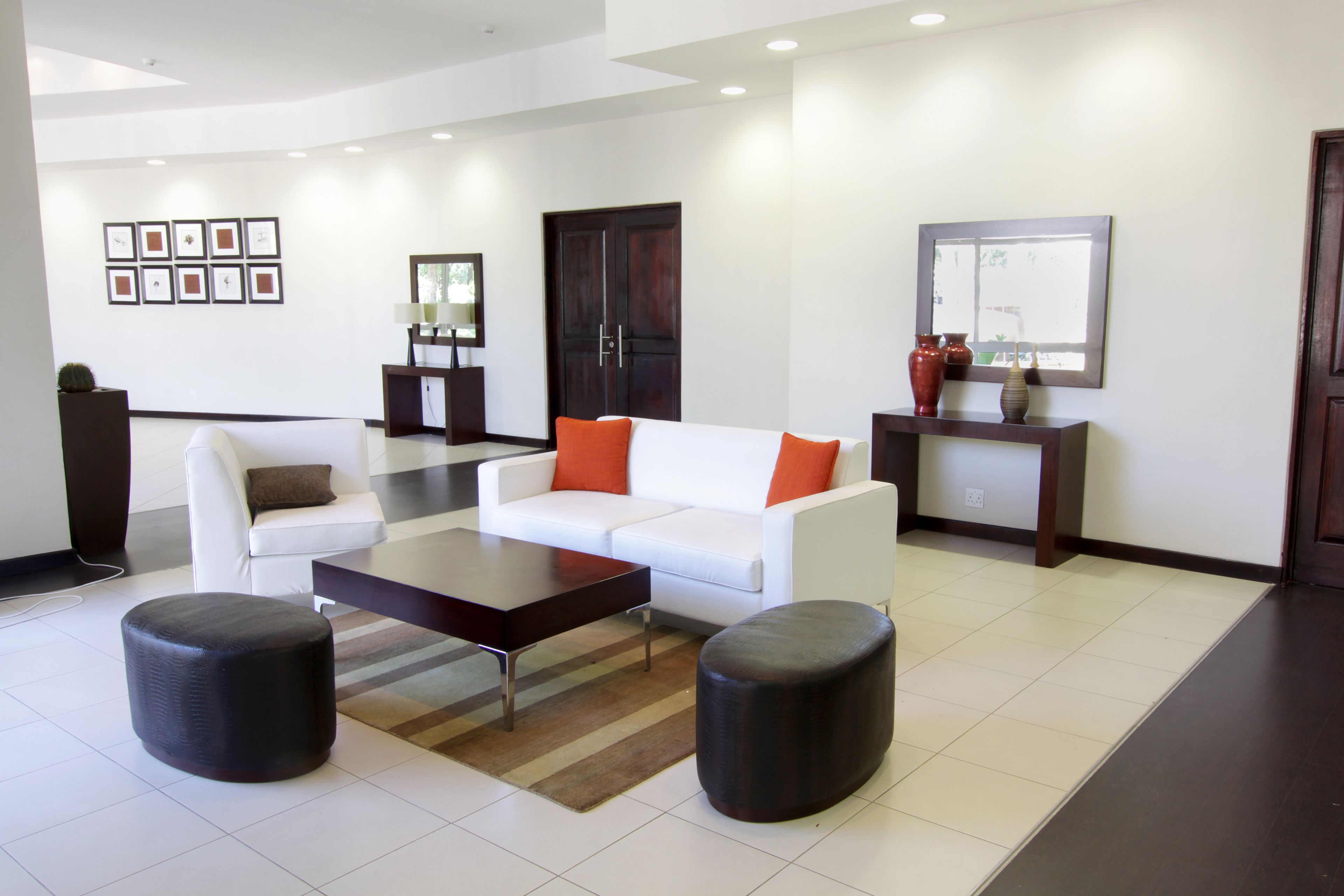 A modern living room with a white sofa, two black ottomans, a coffee table, and a dark wooden door.