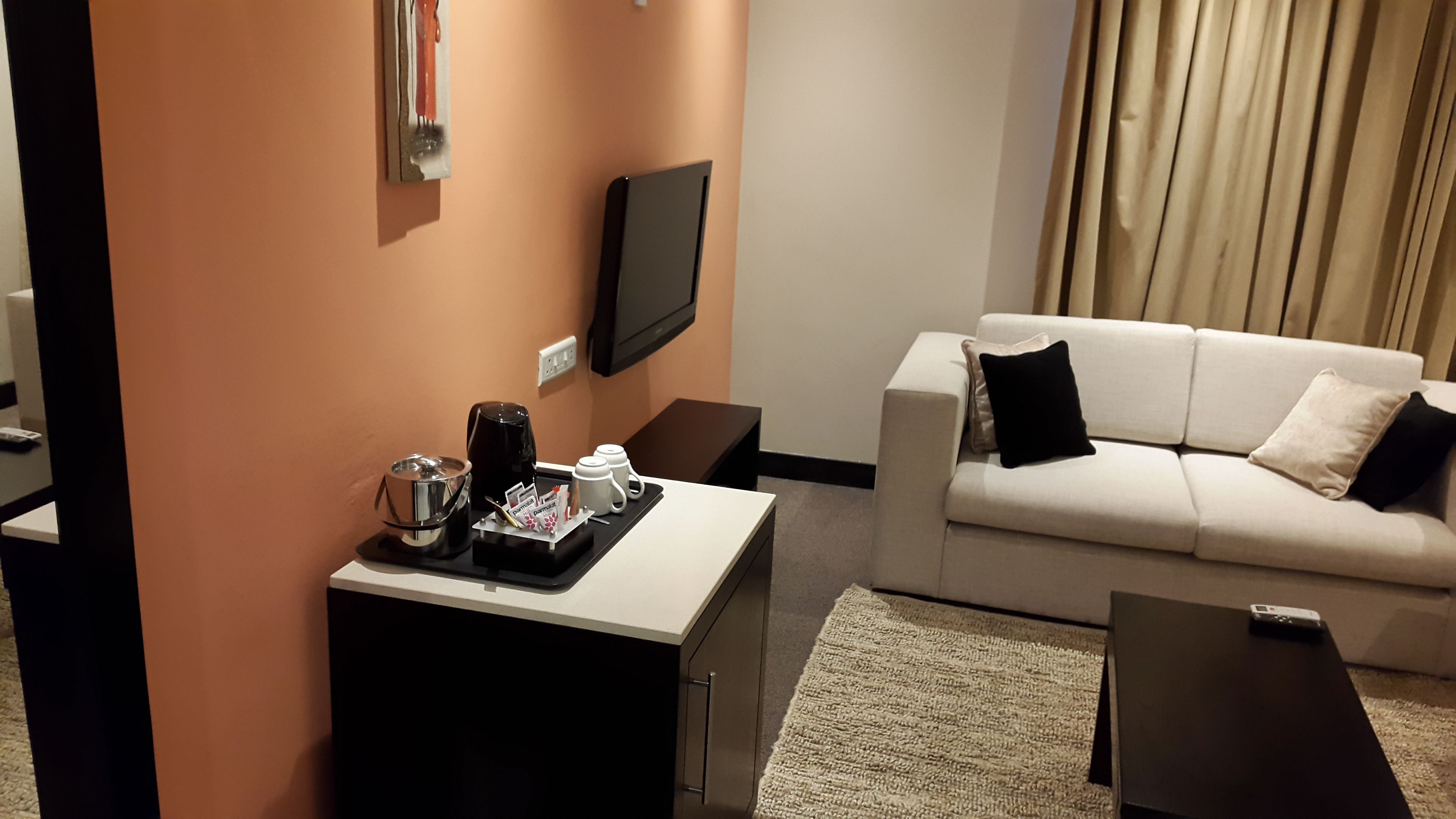 Habitación de hotel con sofá, mesa de centro, televisor y una mesita con cafetera y tazas.
