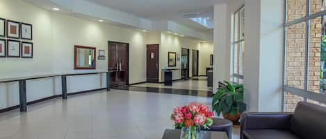 A spacious lobby with a reception desk, a seating area with a sofa and a coffee table, and a large window with a brick wall view.