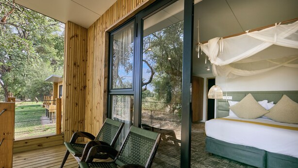 A bedroom with a large window, a bed with white bedding, and a canopy. - Cresta Marang Gardens (Francistown)